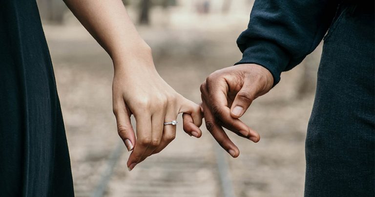 Man and woman holding pinkies, woman wearing engagement ring