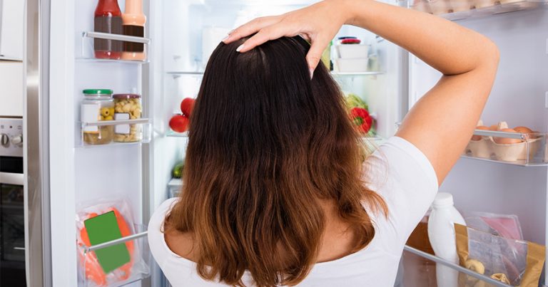 Woman confused standing in front of open fridge