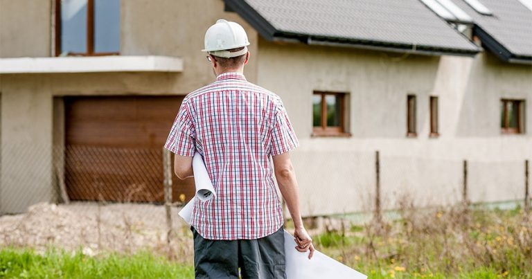 Man with hard hat and blue print standing outside a house