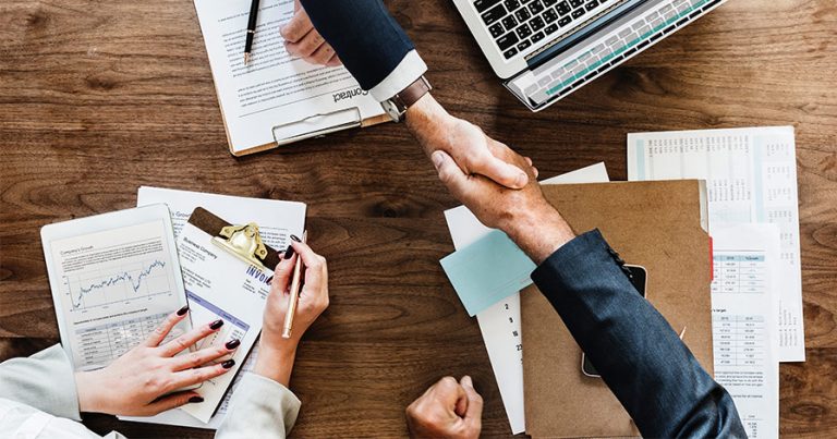 Three people working at a table and shaking hands