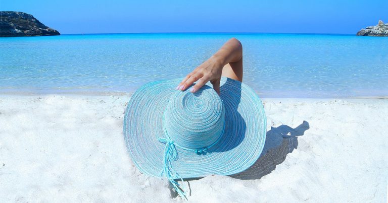 Woman with blue sunhat lying on the beach in the sunshine