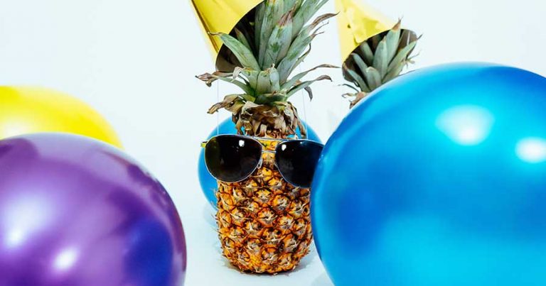 A pineapple wearing a party hat, surrounded by balloons.