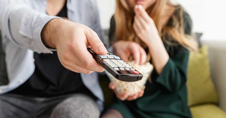A couple eating popcorn and watching a movie at home