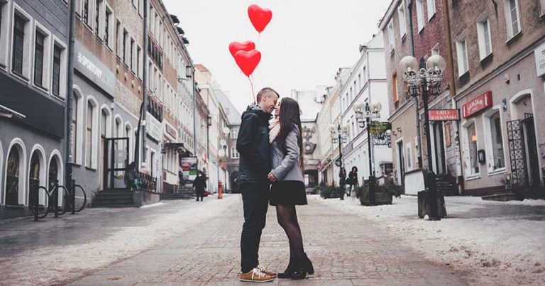 A couple kissing in the street, holding heart-shaped balloons