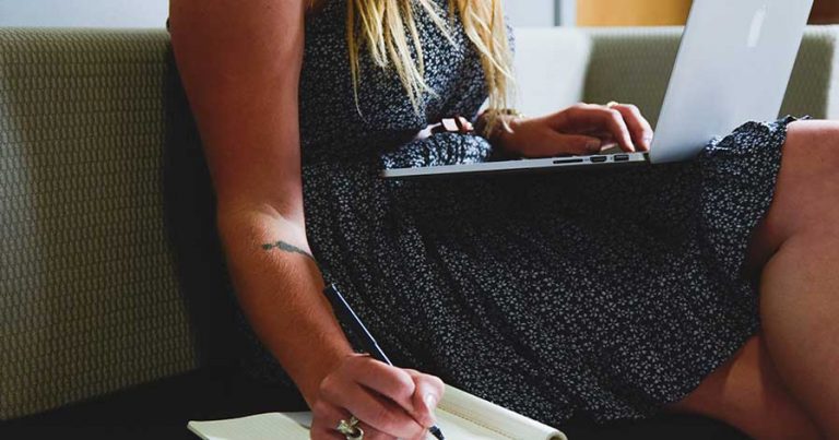 A woman takes notes while reading on her laptop