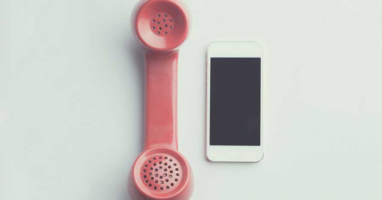 An apple phone on a table beside a landline phone