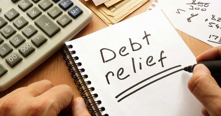 Someone writing about debt relief on a notepad, with a calculator nearby