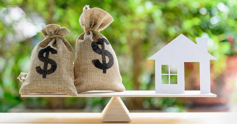Two bags of money and a paper house on a scale