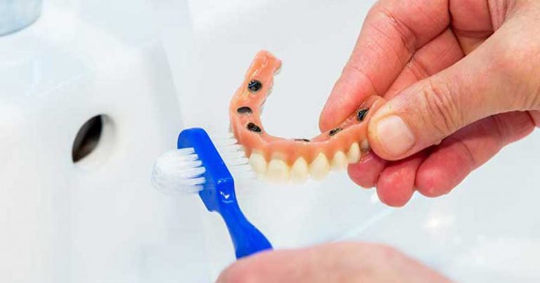 Someone cleaning dentures with a toothbrush