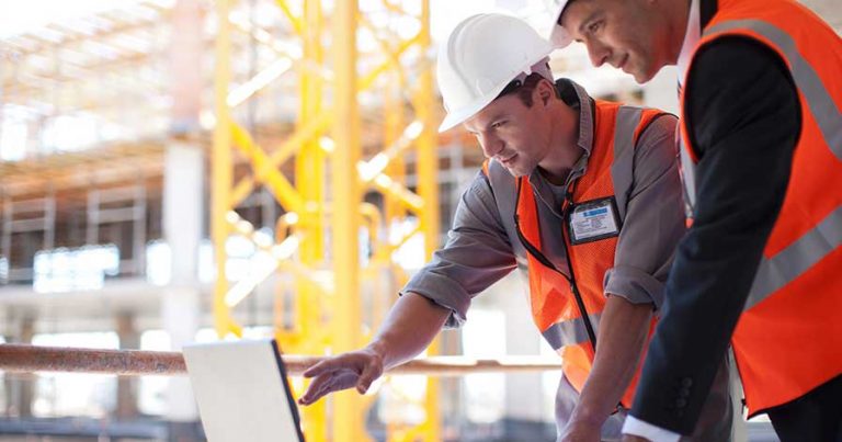 Two construction workers on site, looking at a laptop