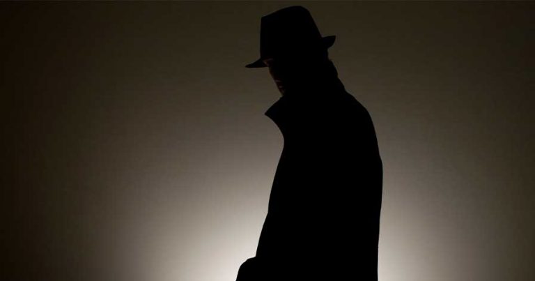 A dark image of a man wearing a jacket and fedora.