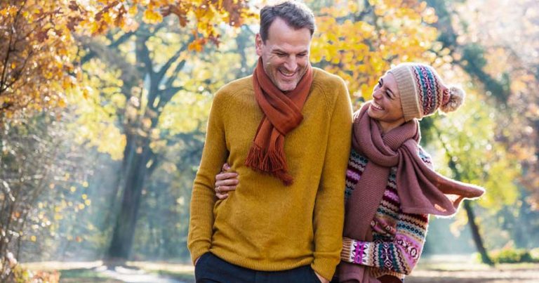A man and a women outside near orange and yellow trees.