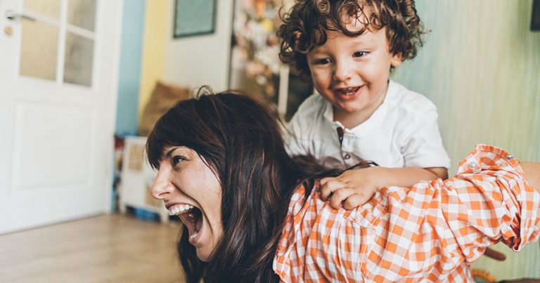 A woman giving a young child a piggy back ride.