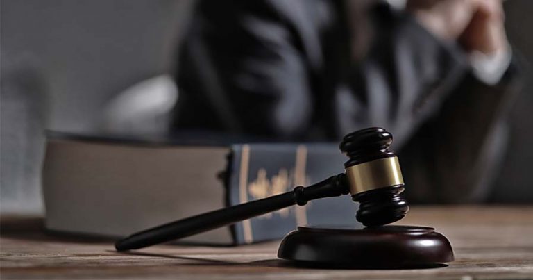 A lawyer in a suit sitting behind a gavel on a table.