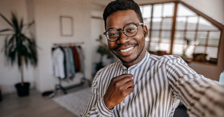 A man smiling while wearing glasses and a button-up shirt with brown stripes.