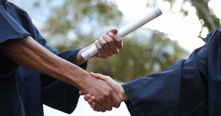 A student and a teacher shaking hands while the student is being given their diploma.