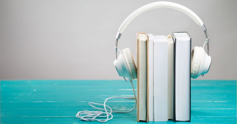 Three books lined up side by side on a blue table, with a pair of white headphones on top of them.