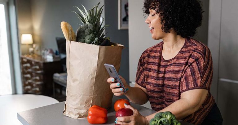 A woman looking at her groceries and phone.