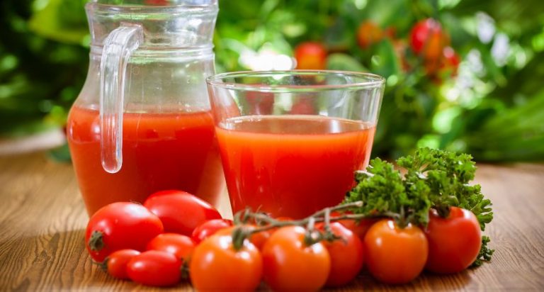 A glass of tomato juice with tomatoes around it.